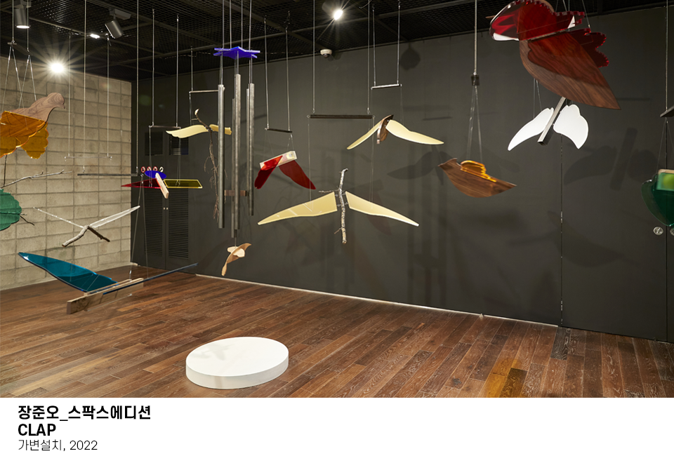 아크릴판과 나무 판자로 다양한 새를 형상화한 조형물이 천장에 매달려 있는 모습이다. 이미지 하단에는 장준오 CLAP 스팍스에디션, 가변설치, 2022 라고 쓰여져 있다.